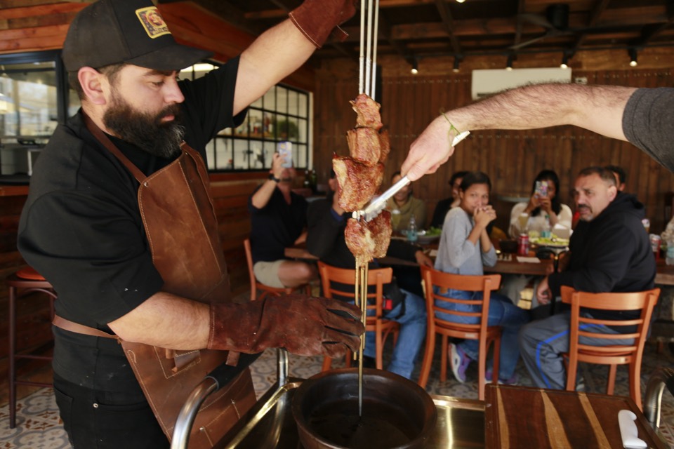 Grill master in a leather apron holding a skewer of grilled meat in a restaurant