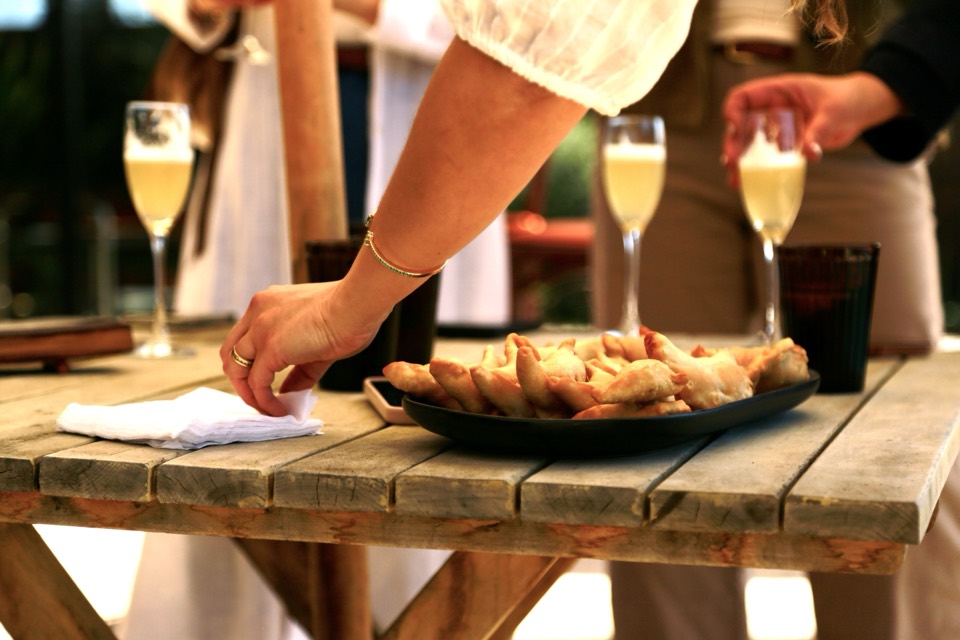 Plate of freshly baked empanadas on a wooden table beside glasses of sparkling wine