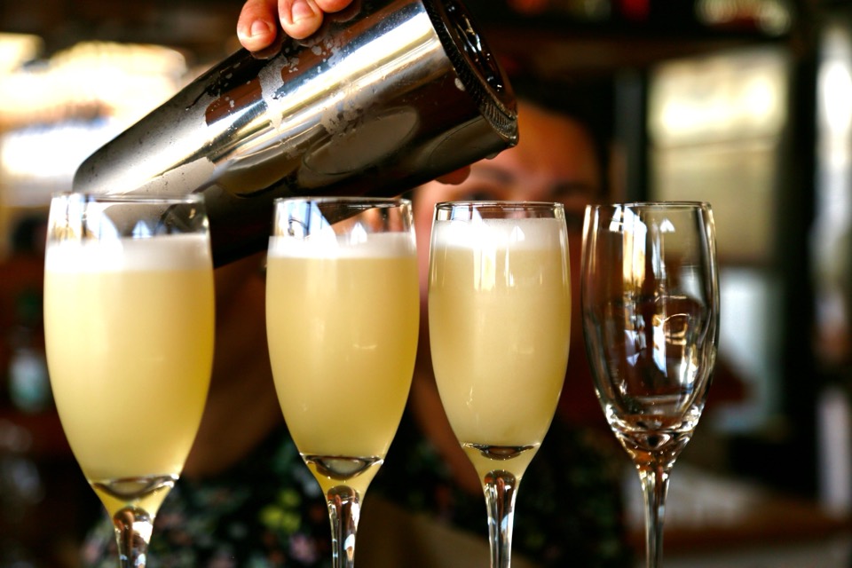 Bartender pouring pisco sours from a shaker into tall glasses