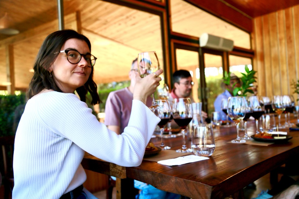 Traveler holding a wine glass at a long table set with a row of tasting glasses