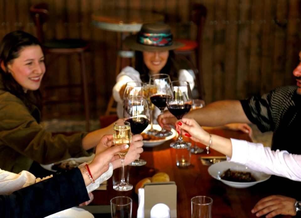 Travelers raising wine glasses in a toast around a wooden table
